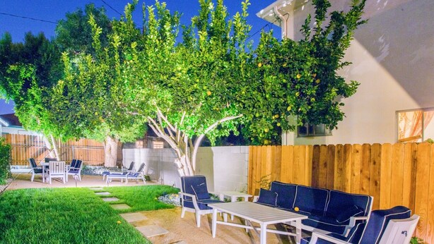 A backyard with a patio area, including a table and chairs, surrounded by a wooden fence and a tree. - City Escape Living (Burbank)