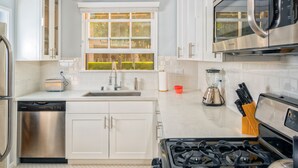 A modern kitchen with white cabinets, stainless steel appliances, a window with a view, and a gas stove. - City Escape Living (Burbank)