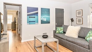 A living room with a grey sofa, a small wooden table, and a bowl on it. There are two posters on the wall, one of a building and one with the text "Los Angeles". - City Escape Living (Burbank)