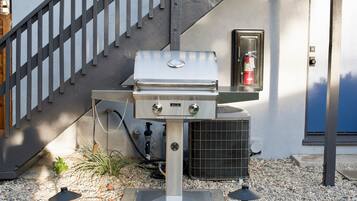 An outdoor grill setup with a fire extinguisher, an air conditioning unit, and a staircase.