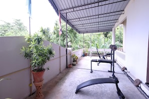 A covered outdoor area with a bench, exercise equipment, and potted plants.