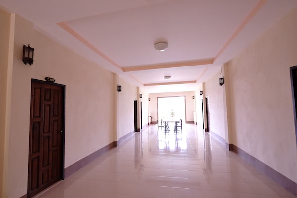 A hallway with a polished floor, a wooden door with a sign, and wall-mounted lights.