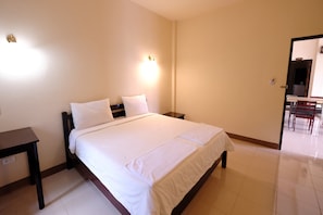 A neatly made bed with white linens in a room with a small table and a chair.