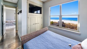 A bedroom with a large window offering a beach view, a bed with a blue quilt, and a wicker bench.