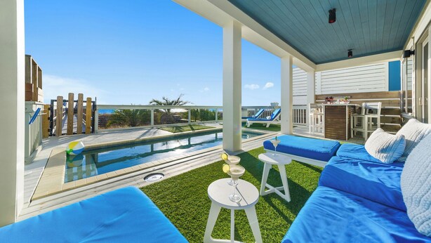 A poolside area with a view of the ocean, a pool, and outdoor seating.