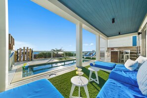 A poolside area with a view of the ocean, a pool, and outdoor seating.