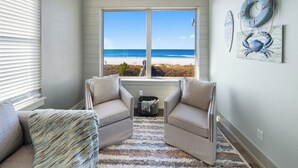 A room with a view of the beach, two armchairs, a rug, and wall art.