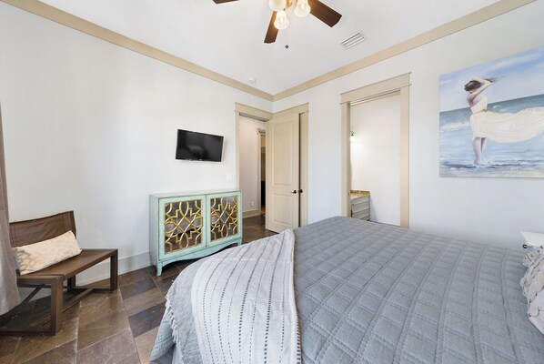 A bedroom with a bed, a bench, a TV, and a painting of a beach scene.