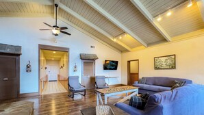 A spacious living area with a wooden ceiling, a ceiling fan, a flat-screen TV, a sofa, and a coffee table.