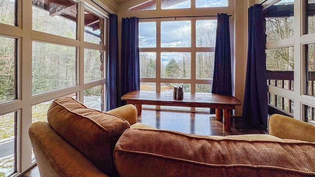 A cozy room with a large window, a wooden table, and a brown sofa.