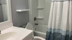 A bathroom with a white sink, a mirror, a toilet, and a shower with a blue and white shower curtain.