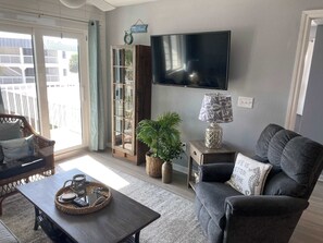 A living room with a sofa, a coffee table, a TV, a bookshelf, and a window with curtains. - Gulf Shores Plantation Resort 4307 (Gulf Shores)