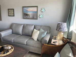 Ein graues Sofa mit Kissen, ein Korbsessel, ein Tisch mit Lampe und dekorative, sternförmige Objekte an der Wand.
