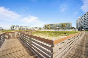 A wooden boardwalk leading to a beachfront hotel with multiple buildings, a sandy area, and palm trees. - Gulf Shores Plantation Resort 4307 (Gulf Shores)