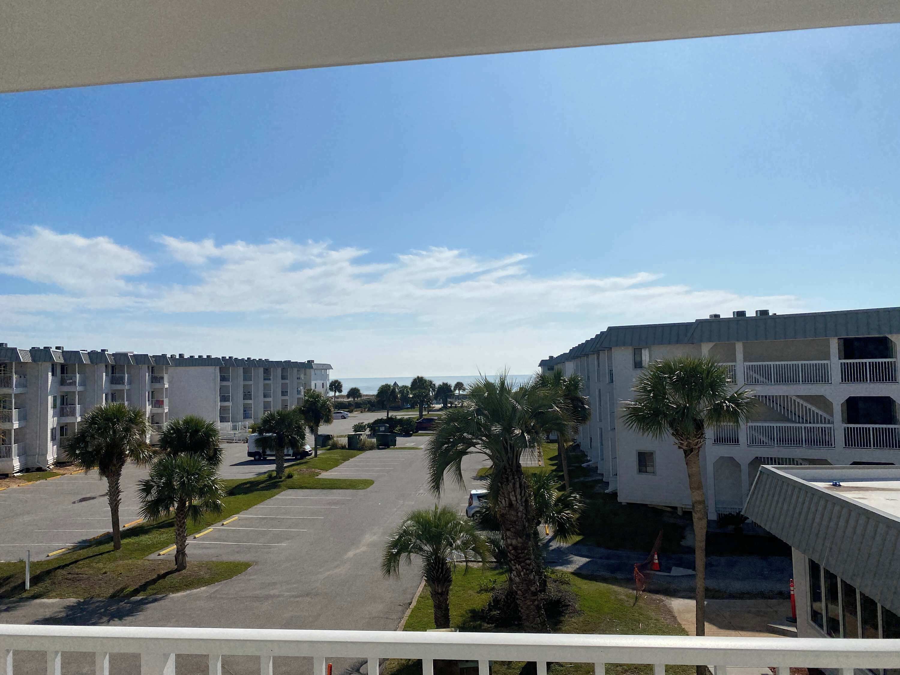 A view of a hotel with multiple buildings, a parking lot, and palm trees.
