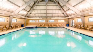 An indoor swimming pool with a high ceiling, multiple windows, and lounge chairs along the sides.