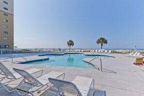 A pool area with lounge chairs and a clear view of the ocean.