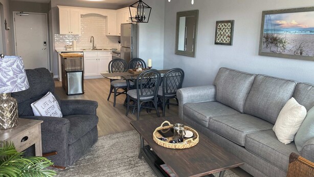 A modern living room with a grey sofa, a coffee table, and a dining area with a table and chairs.