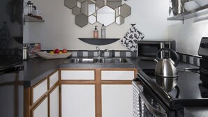 Una cocina compacta con piso a cuadros blanco y negro, un microondas, una tetera y un lavamanos.