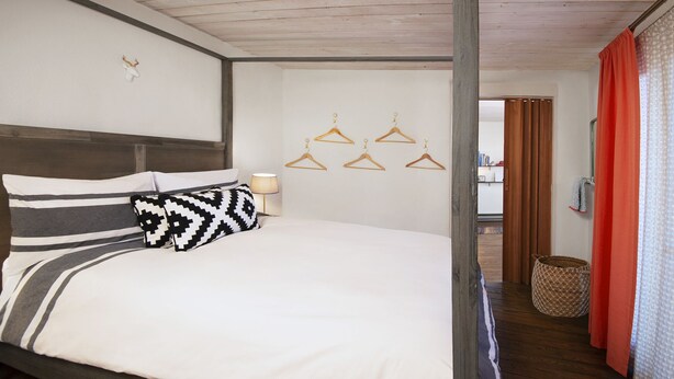 Un dormitorio con cama, cabecera, lámpara de pared y suelo de madera.
