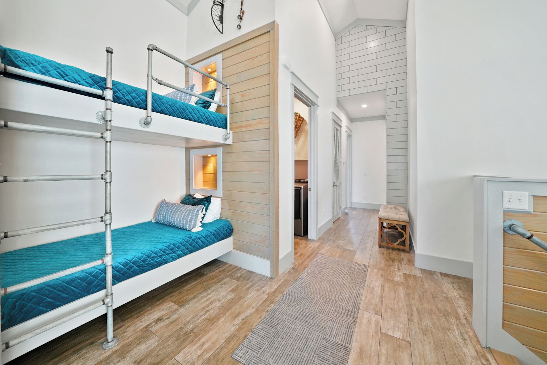 A multi-level bunk bed room with a wooden floor, a small stool, and a visible laundry area.