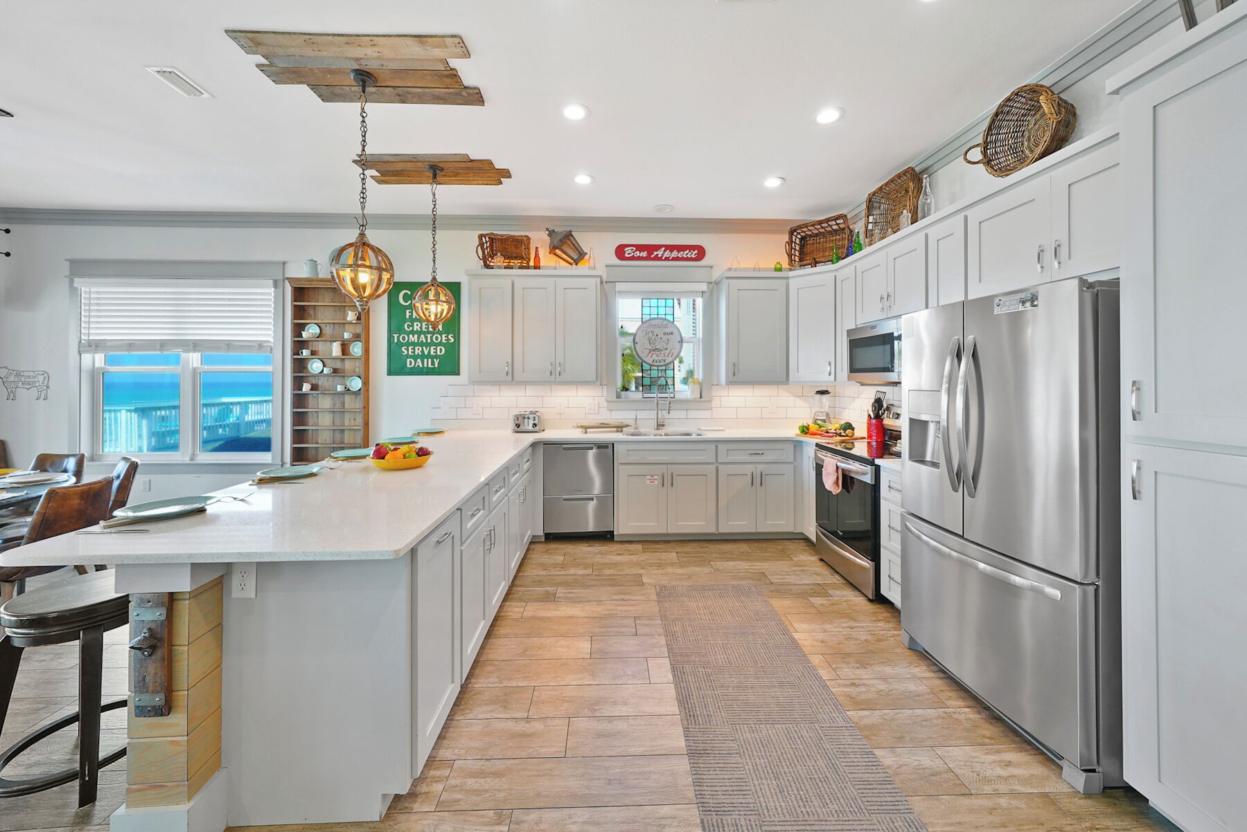 A modern kitchen with white cabinetry, a stainless steel refrigerator, and a large island with a bowl of fruit.