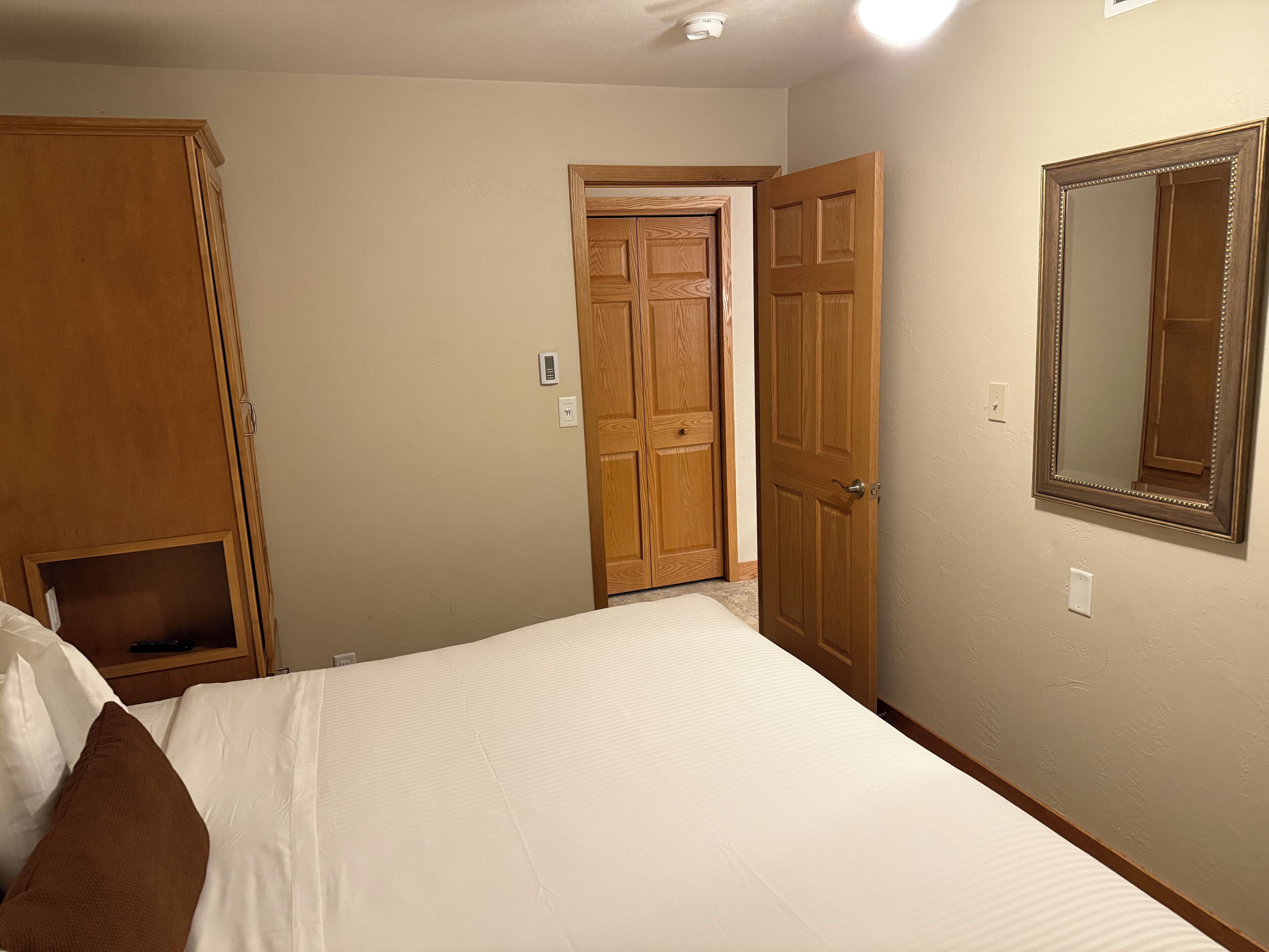 Une chambre à coucher avec un lit, une armoire en bois et une porte dotée d’un miroir.