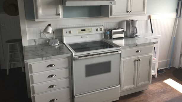 Une cuisine avec des meubles blancs, une cuisinière, un grille-pain et une machine à café.
