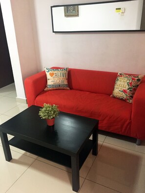 A red sofa with two decorative pillows, a small black table with a potted plant, and a framed picture on the wall. - iCheck Homestay Putrajaya (Putrajaya)