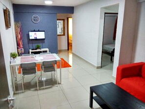 A dining area with a table and chairs, a TV mounted on the wall, and a red sofa in the foreground. - iCheck Homestay Putrajaya (Putrajaya)