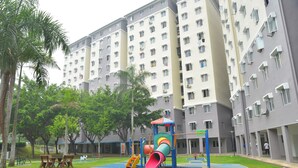A playground with a slide and climbing structures, surrounded by a grassy area and palm trees, with a residential building in the background. - iCheck Homestay Putrajaya (Putrajaya)
