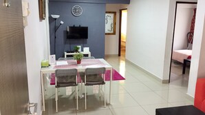 A dining area with a table, chairs, a potted plant, a clock, and a TV on the wall. - iCheck Homestay Putrajaya (Putrajaya)