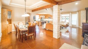 A spacious living area with a dining table, wooden chairs, a fireplace, and a kitchen in the background.
