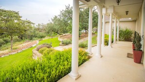 A covered porch with white columns, a garden with various plants, and a view of the surrounding landscape.