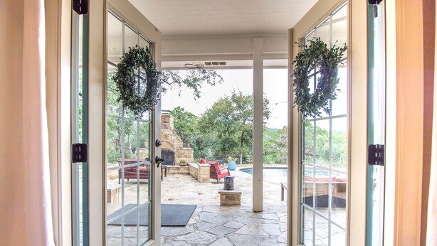 A stone-floored patio with outdoor furniture, a fire pit, and a view of a swimming pool and trees.