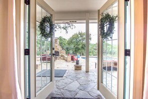 A stone-floored patio with outdoor furniture, a fire pit, and a view of a swimming pool and trees. - New! Town & Country Luxury Oasis near Gruene, TX - Private Pool (New Braunfels)