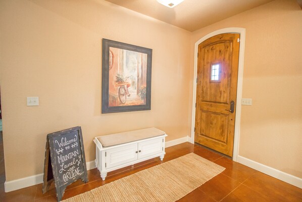 A hallway with a wooden door, a framed painting, a white bench, and a chalkboard sign. - New! Town & Country Luxury Oasis near Gruene, TX - Private Pool (New Braunfels)