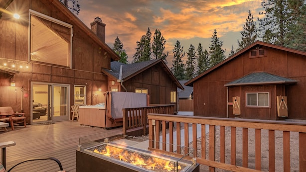 Una cabaña de madera con terraza, un pozo de fuego y un jacuzzi.