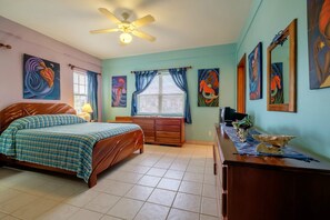 Ein Schlafzimmer mit Bett, Schreibtisch, Stuhl, Deckenventilator und Bildern an den Wänden.