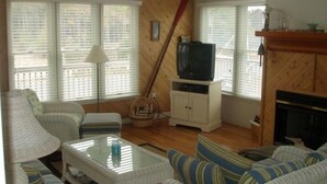 A cozy living room with a television on a cabinet, a fireplace, and a large window with blinds. - Pet friendly  See specials in the description section (Nags Head)