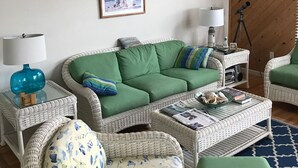 A cozy living room with a green sofa, wicker chairs, a coffee table, and a telescope on a tripod. - Pet friendly  See specials in the description section (Nags Head)