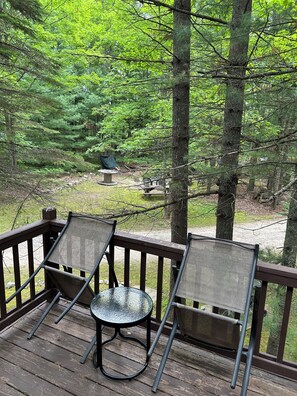 Une terrasse en bois avec deux chaises et une table, donnant sur une zone boisée.