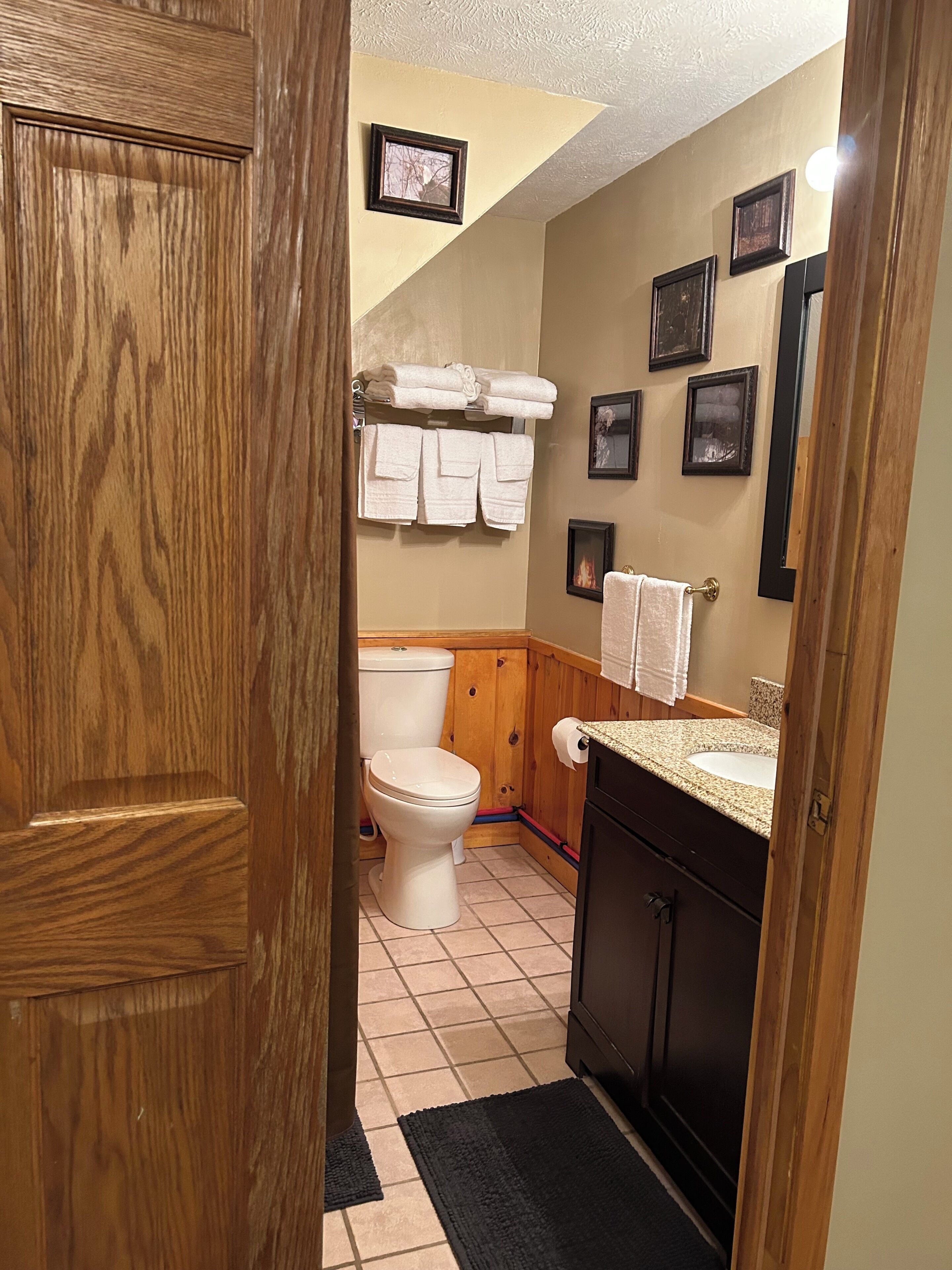 A bathroom with a toilet, sink, wooden cabinets, and a towel rack with towels.