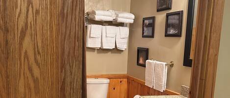 A bathroom with a toilet, sink, wooden cabinets, and a towel rack with towels.