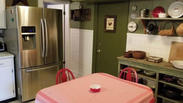 A kitchen with a stainless steel refrigerator, a red table with a bowl, and various kitchenware on shelves. - Awesome Flat Top Farmhouse - Ashwood Rentals (Flat Top)