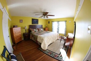 A bedroom with a bed, dresser, nightstand, chair, and a ceiling fan.