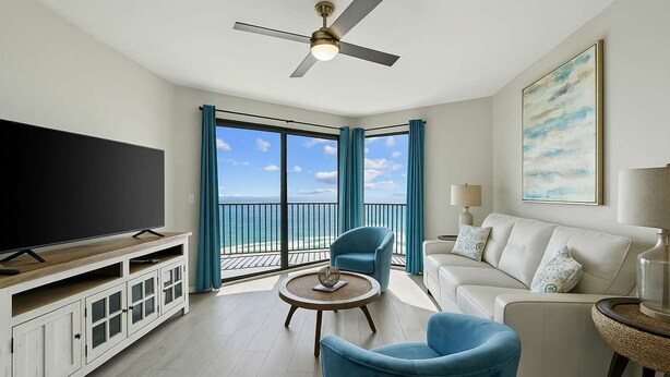A spacious living room with a large flat-screen TV, a ceiling fan, and a balcony with a view of the ocean. - Phoenix VII 71113 by ALBVR - Upgraded Beautiful Beachfront Condo Could be Yours! (Orange Beach)