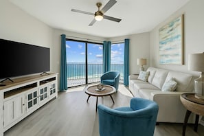 A spacious living room with a large flat-screen TV, a ceiling fan, and a balcony with a view of the ocean. - Phoenix VII 71113 by ALBVR - Upgraded Beautiful Beachfront Condo Could be Yours! (Orange Beach)