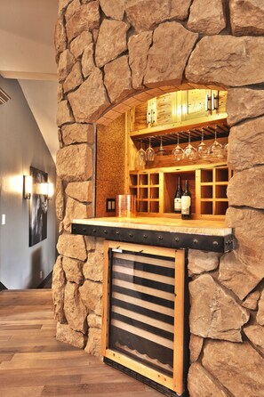 A stone wall bar area with wooden shelves, wine glasses, and bottles.