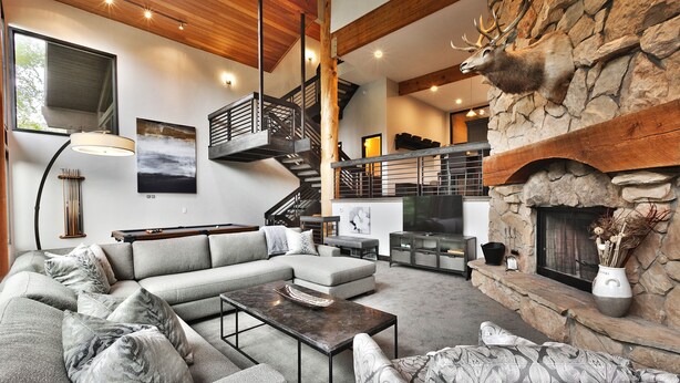 Una sala de estar moderna con chimenea de piedra, un sofá seccional grande, una escalera de madera y un televisor de pantalla plana.